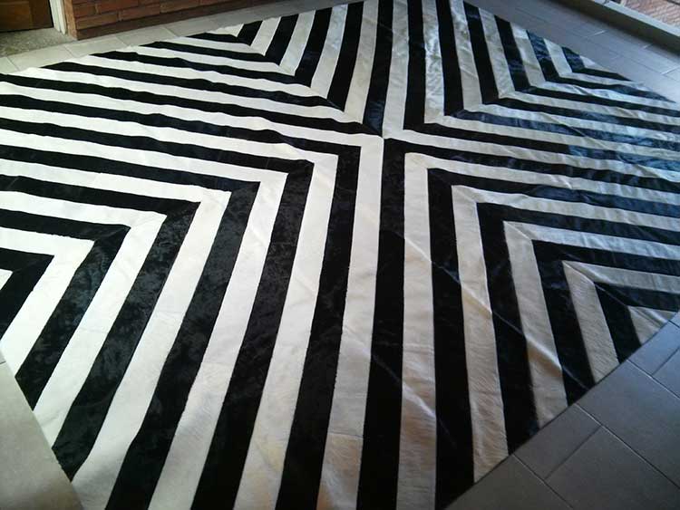 Full view of a cowhide patchwork rug in black and white wide strips, merging in the center. Each strip was hand-cut specially for this project.