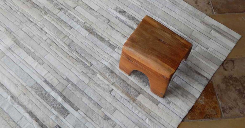 White and grey patchwork cowhide rug with wooden handmade stool on it