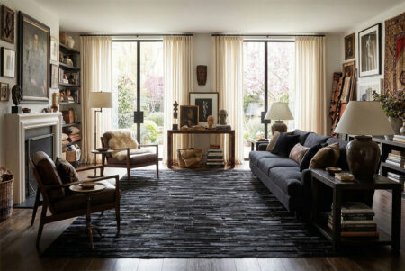 253-Black-Stripes-Patchwork-Cowhide-Rug-in-Maximalist-Living-Rooom A sophisticated, maximalist living room featuring a black striped patchwork cowhide rug centered on the wooden floor. There's a dark cotton sofa and vintage armchairs. Natural light illuminates the eclectic wall art and dark decor.