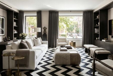 Black and White Chevron Patchwork Cowhide Rug in modern NY living room 278 Modern NYC apartment living room featuring a large black and white chevron area rug, a white sofa, a large fabric pouf coffee table, and dark wood built-in shelves.