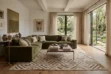 Beige and white geometric patchwork cowhide rug styling in a sunlit luxury living room in Málaga, featuring a green velvet sofa, natural wood floors, and open garden views.