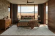 White Diamond Cowhide Area Rug with a geometric patchwork pattern on dark wood floors in a modern bedroom setting with a large window view of rolling hills.