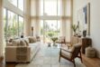 Sun-drenched modern living room featuring a large white patchwork cowhide rug, neutral furniture, and floor-to-ceiling windows with sheer curtains.