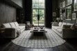 A luxurious, moody living room featuring a large, round patchwork cowhide rug with a grey and beige houndstooth pattern. The space includes dark-toned walls, high ceilings, dark wooden floors, two light linen sofas facing each other, a rustic wood coffee table, and an eclectic armchair. A curated gallery wall of art hangs on the right, and large, tall glass doors open to a lush green garden in the background, letting in natural light.