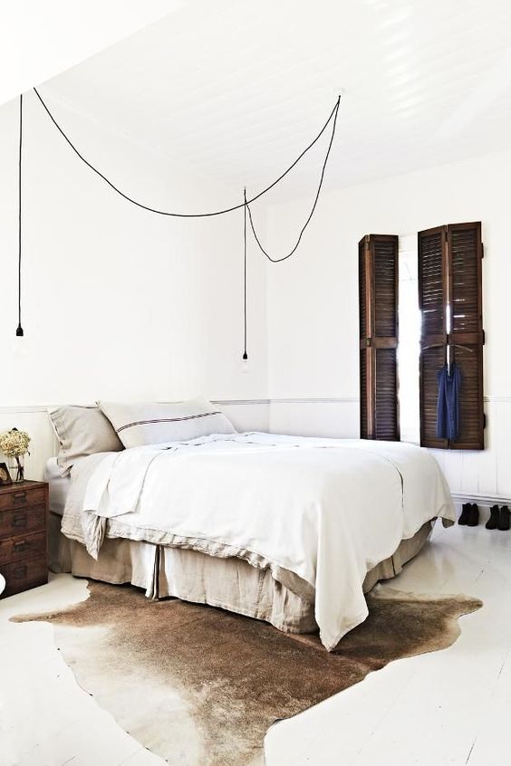 industrial master bedroom with a big white bed, hanging light bulbs and a beige cowhide area rug