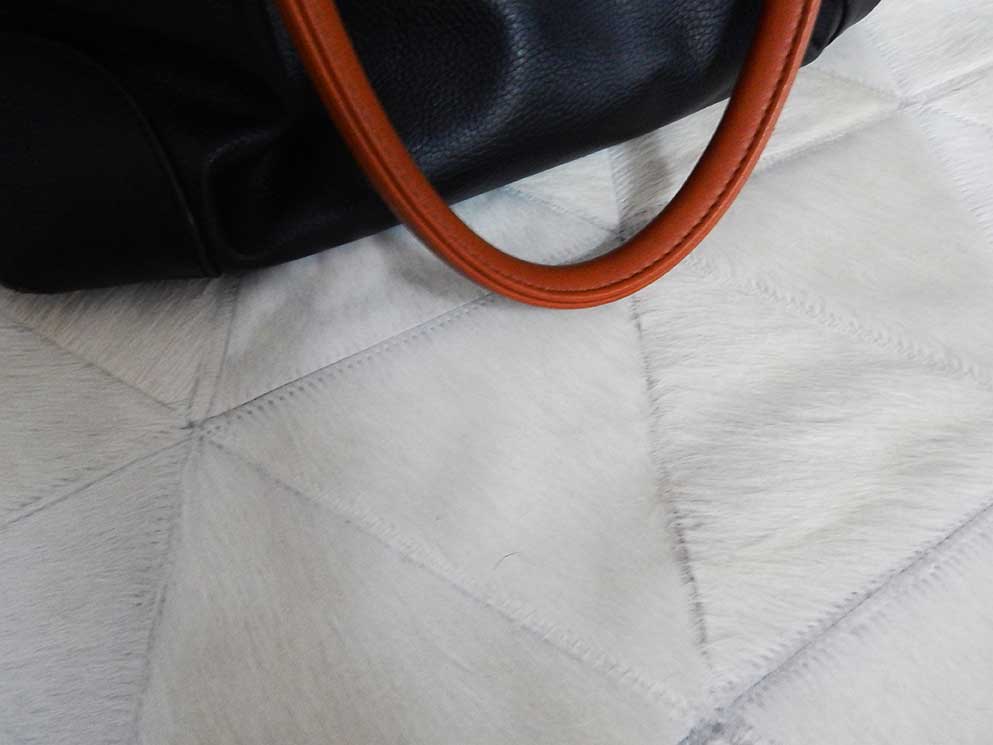 Close up of our kata patchwork cowhide rug with a black leather bag with caramel stripes resting on it
