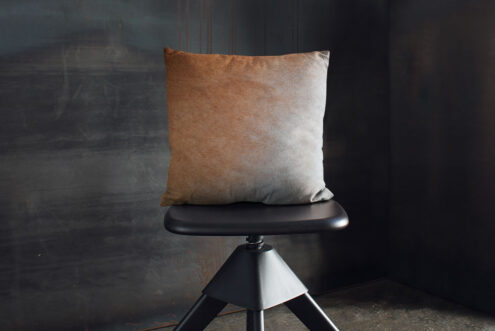 08-beigegradient-50x50-04 Beige Gradient Cowhide Pillow on an industrial black stool and black walls