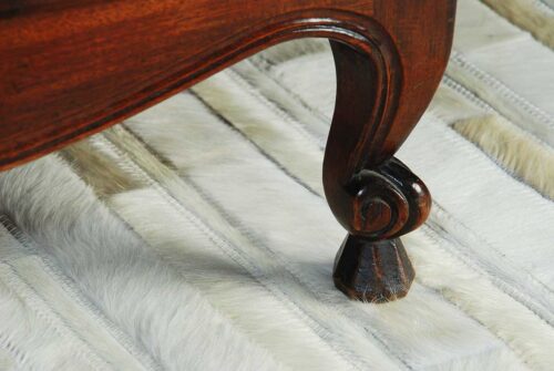 Detail of white patchwork cowhide rug in stripes with antique furniture