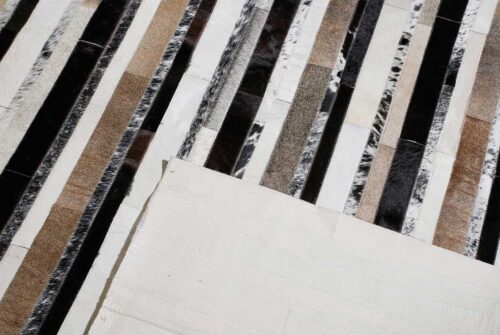 Detail of a black, beige and black with salt and pepper cowhide patchwork rug designed in stripes