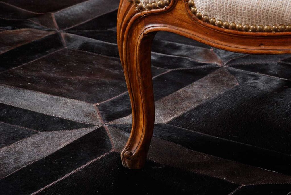 Detail of a chocolate brown patchwork cowhide rug in the cube design with wooden furniture on