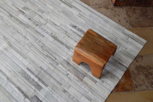 Top view of a gray and white patchwork cowhide rug with wooden stool