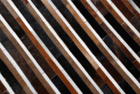 Top detail of black, brown and white patchwork cowhide rug in stripes Top detail of black, brown and white patchwork cowhide rug in stripes