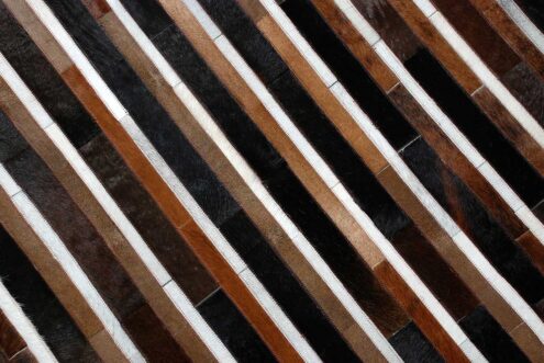 Top detail of black, brown and white patchwork cowhide rug in stripes Top detail of black, brown and white patchwork cowhide rug in stripes