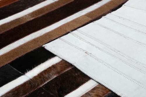 Detail of black, brown and white patchwork cowhide rug in stripes with backing
