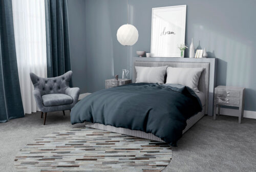 Round taupe gray cowhide patchwork rug in Stripes in a blue bedroom