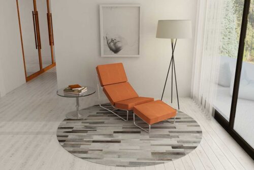 Round gray cowhide patchwork rug designed in stripes in a bright room with orange chaise lounge
