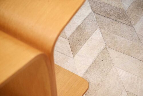 Close up of a Chevron gray cowhide patchwork rug with wooden modern bench