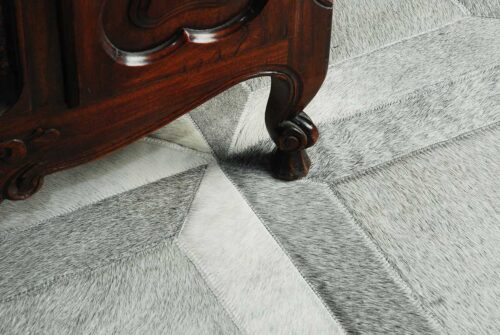Detail of a gray Cube patchwork cowhide rug with antique furniture legs