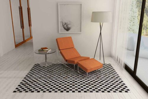 Checkerboard patchwork cowhide rug in black and beige with an orange chaise lounge