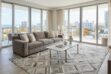 open plan living room in Miami with a big Taupe Diamond cowhide area rug setting the limits for the space. A gray sofa with light cushions and a glass coffee table. Very luminous and fresh