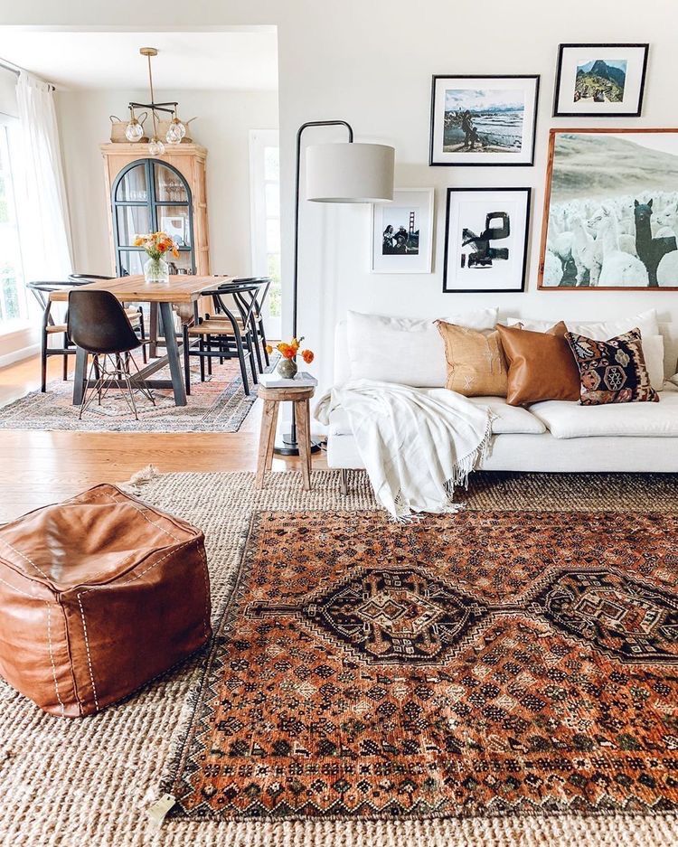 Layered rugs defining the space of the living room, leather pouf and wall art