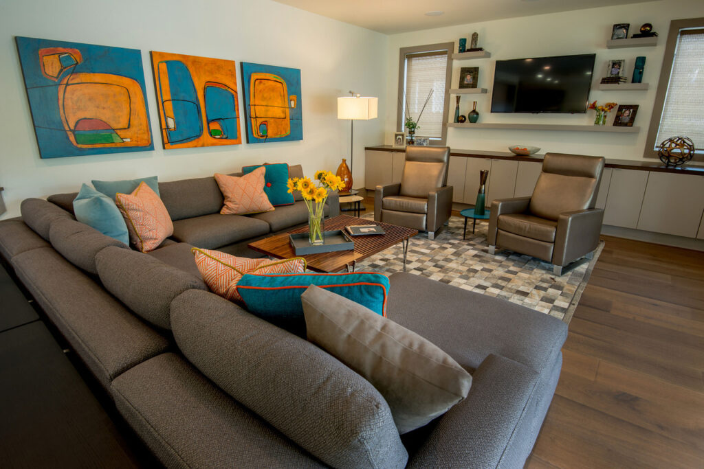 A living room with gray sofa, shiny armchairs and teal and orange details. A Gray and White Squares Patchwork Cowhide Rug by Shine Rugs brings the whole room together