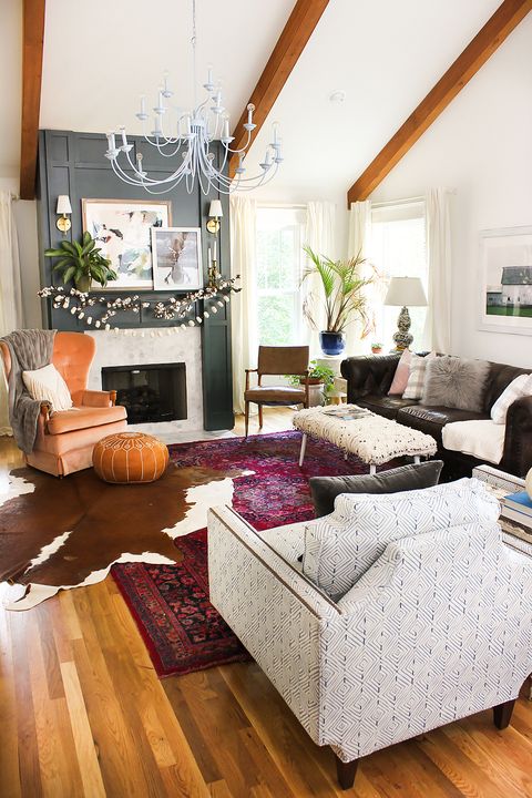 Classic vintage rug in dark purple tones and an overlapped brown and white cowhide rug in a boho styled living room with chandelier