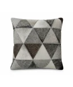 A detailed, frontal photograph of a single square cushion cover made entirely of cowhide patchwork. The front features a precise geometric pattern of hair-on-hide triangles in varying natural shades of light grey, medium grey, and dark taupe, arranged in an alternating, tiled pattern. The individual patches are connected with visible, even grey stitching, and the natural texture of the hair-on-hide is prominent. The cushion is shown against a neutral, plain background.