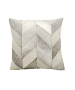 A square decorative throw pillow made of cowhide, featuring a geometric chevron patchwork pattern in natural shades of grey, white, and light beige